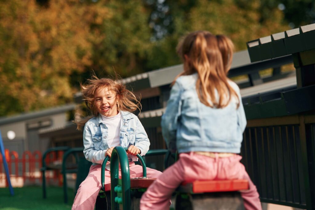 Two girls happily playing on a seesaw in the kindergarten garden