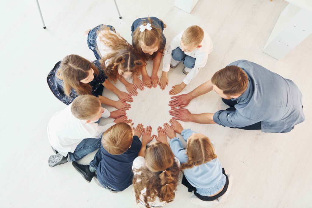 Kindergarten students forming a circle on the floor with their teacher, top-down view