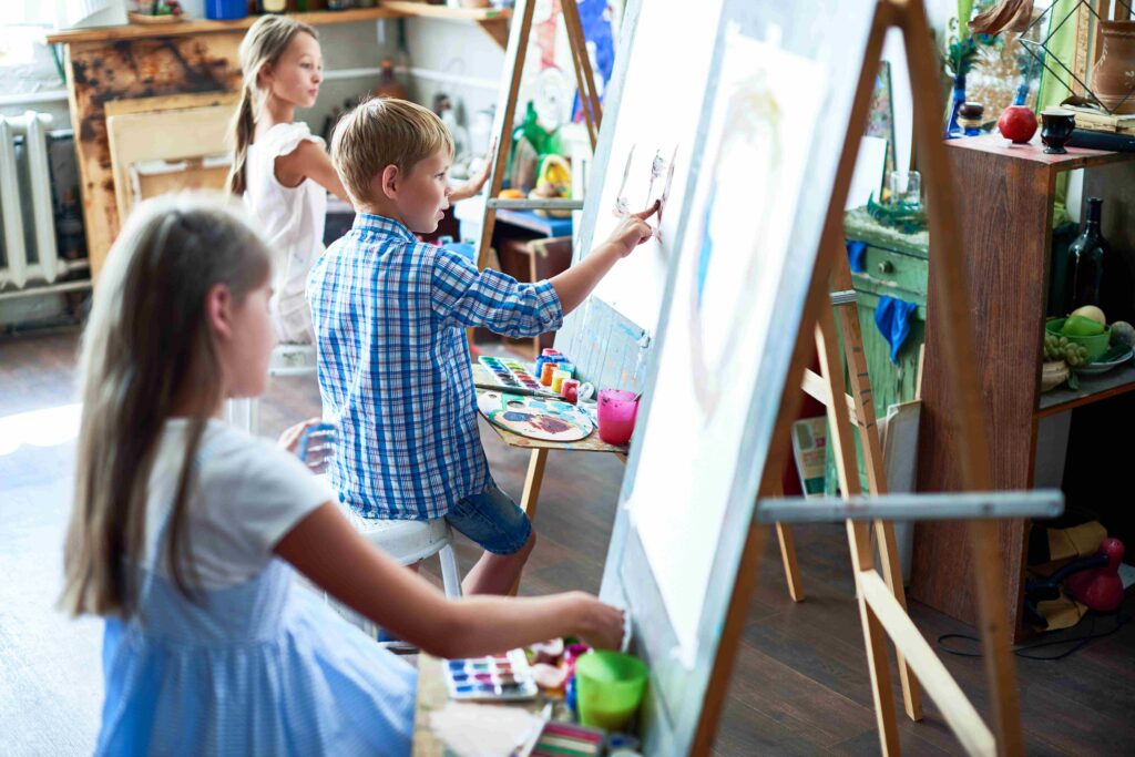 İlkokul sanat dersinde tuval başında resim yapan öğrenciler